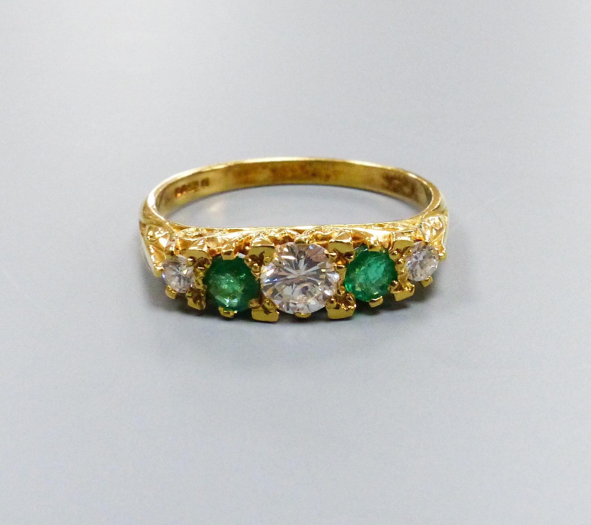 A modern Victorian style 18ct gold, three stone diamond and two stone emerald set half hoop ring, size P, gross weight 3.4 grams.